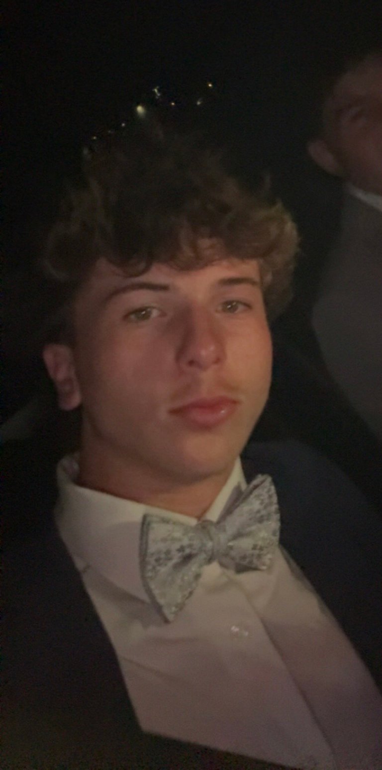 Young man in formal attire with white dress shirt and patterned bow tie against dark background